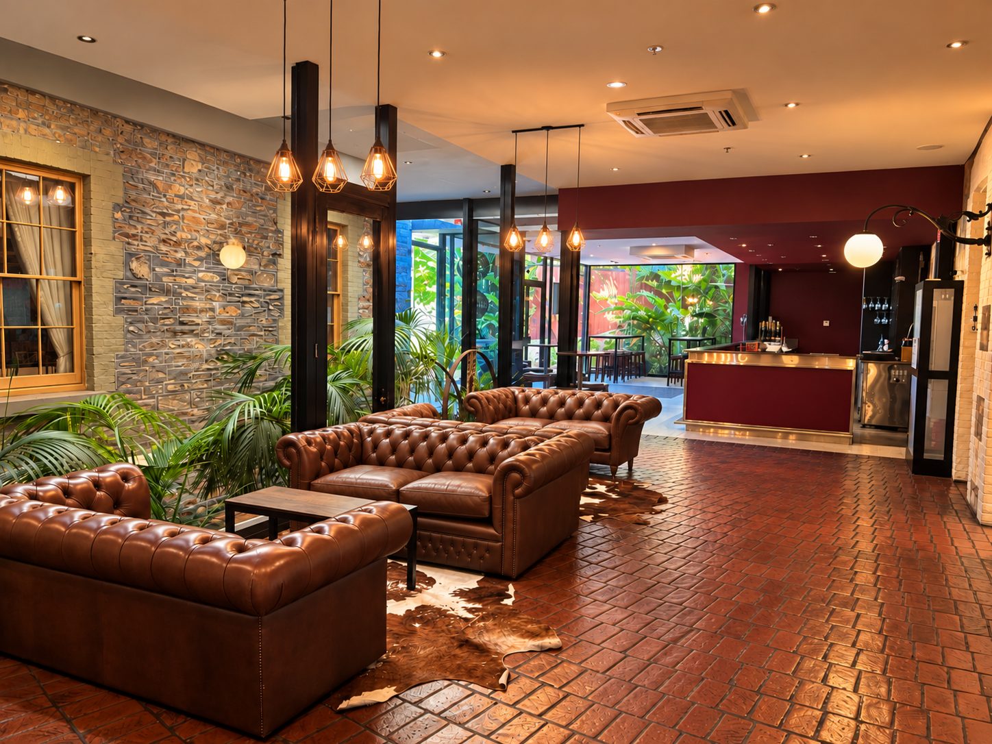 The bar lounge, leather Chesterfield sofas on terracotta tiles with the bar and a planted courtyard beyond
