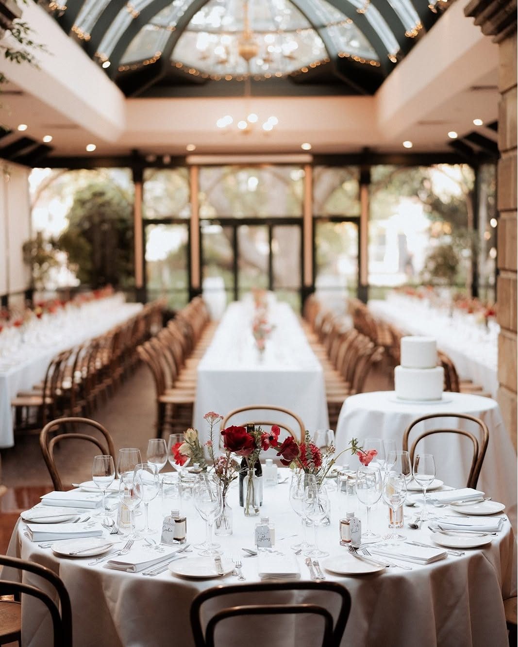 The Conservatory set for a wedding, long and round tables under the glass dome, with the cake on its own table