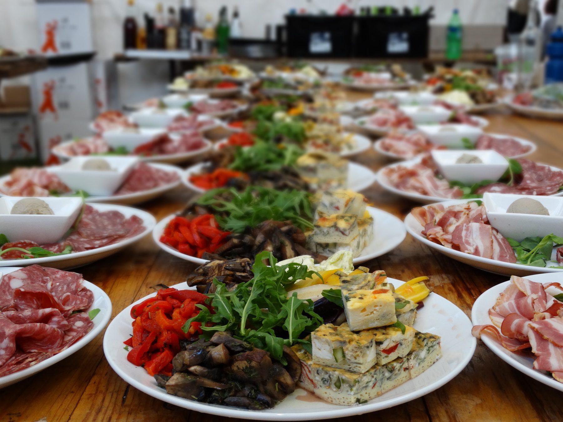 A long table laid end to end with antipasto platters: cured meats, roasted peppers, mushrooms, frittata, rocket and dips