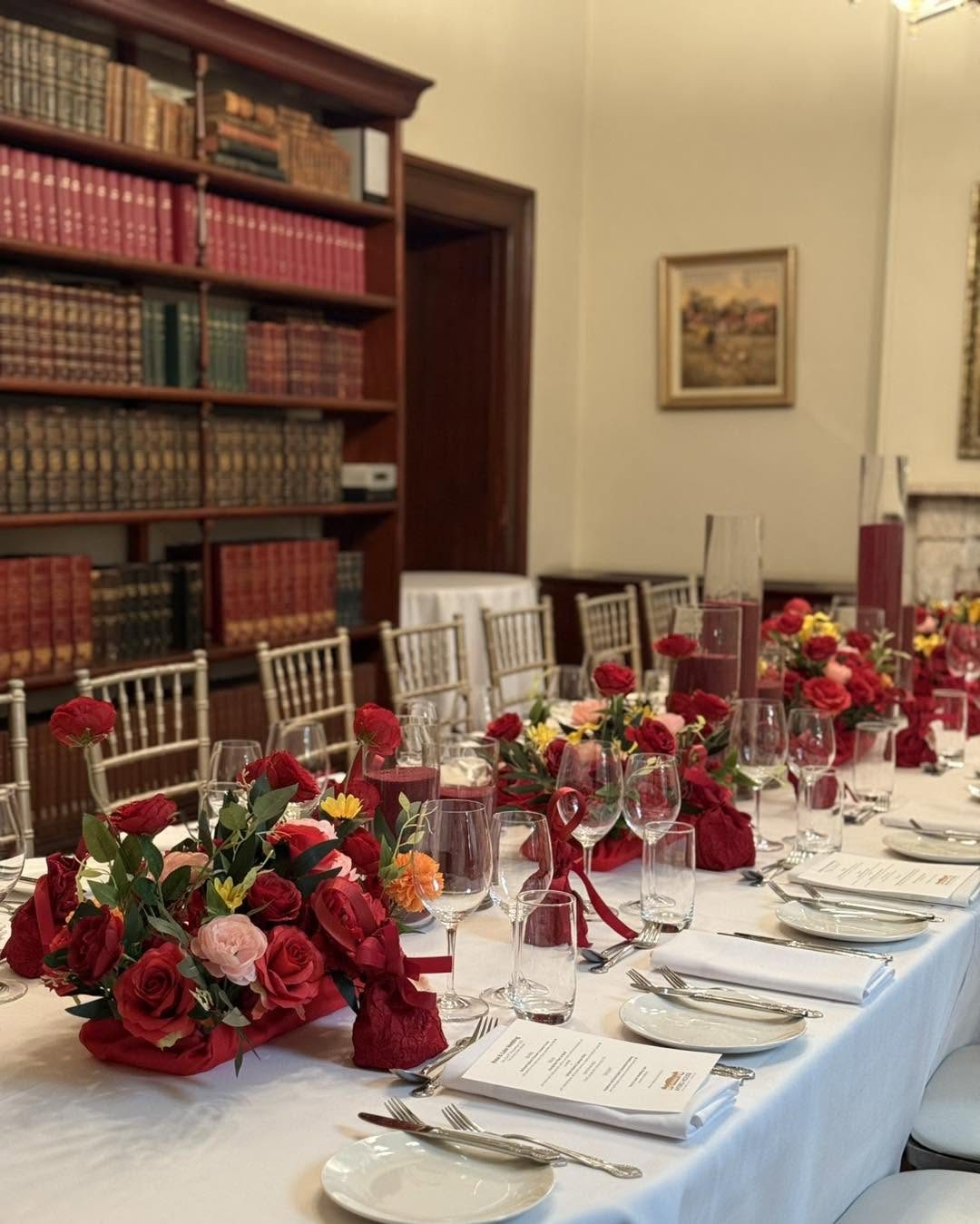 The Library set for a celebration, a long table with red roses beside the bookshelves